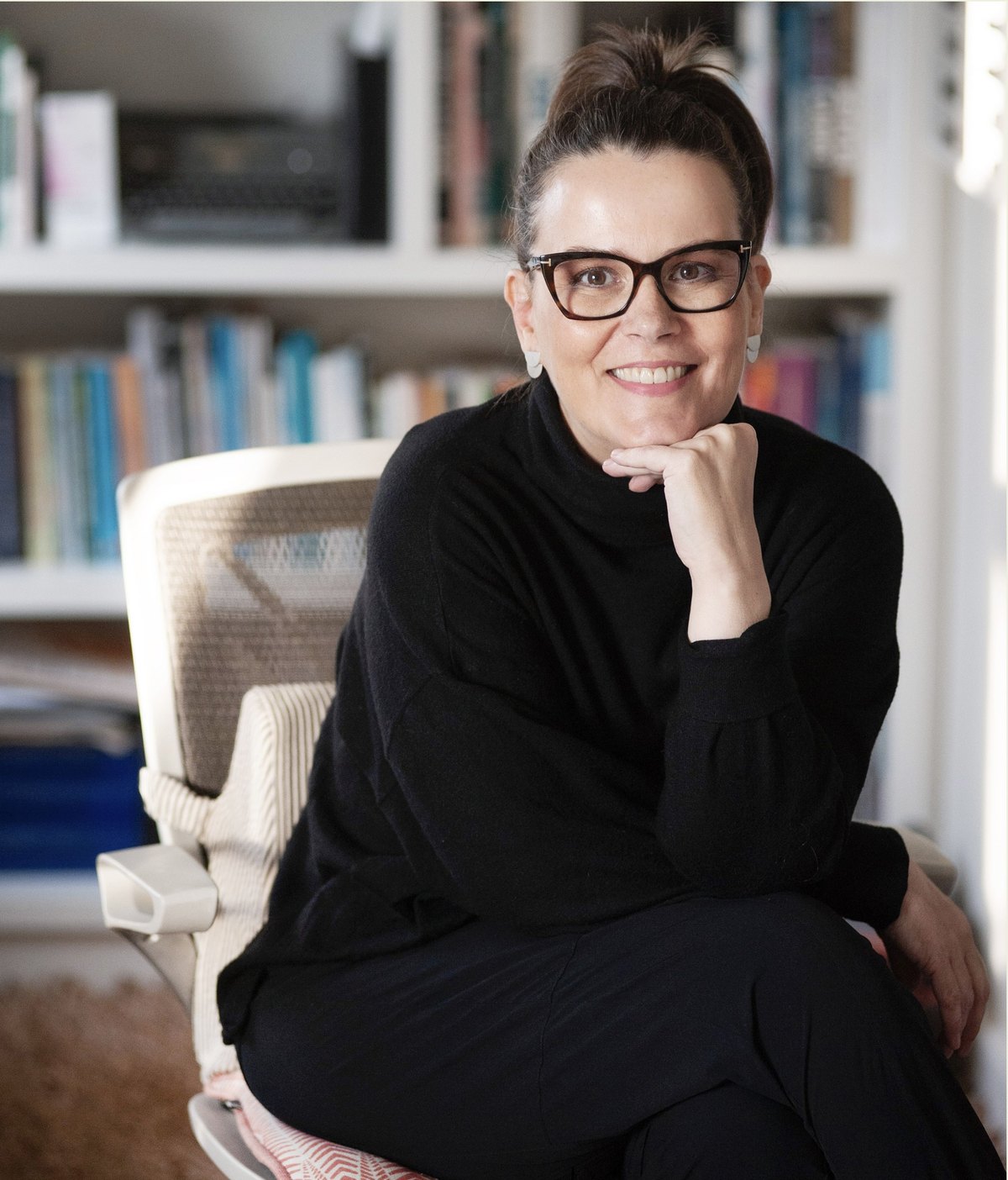 Suzana Kroeff, psicóloga clínica, sentada em seu consultório diante de uma estante de livros